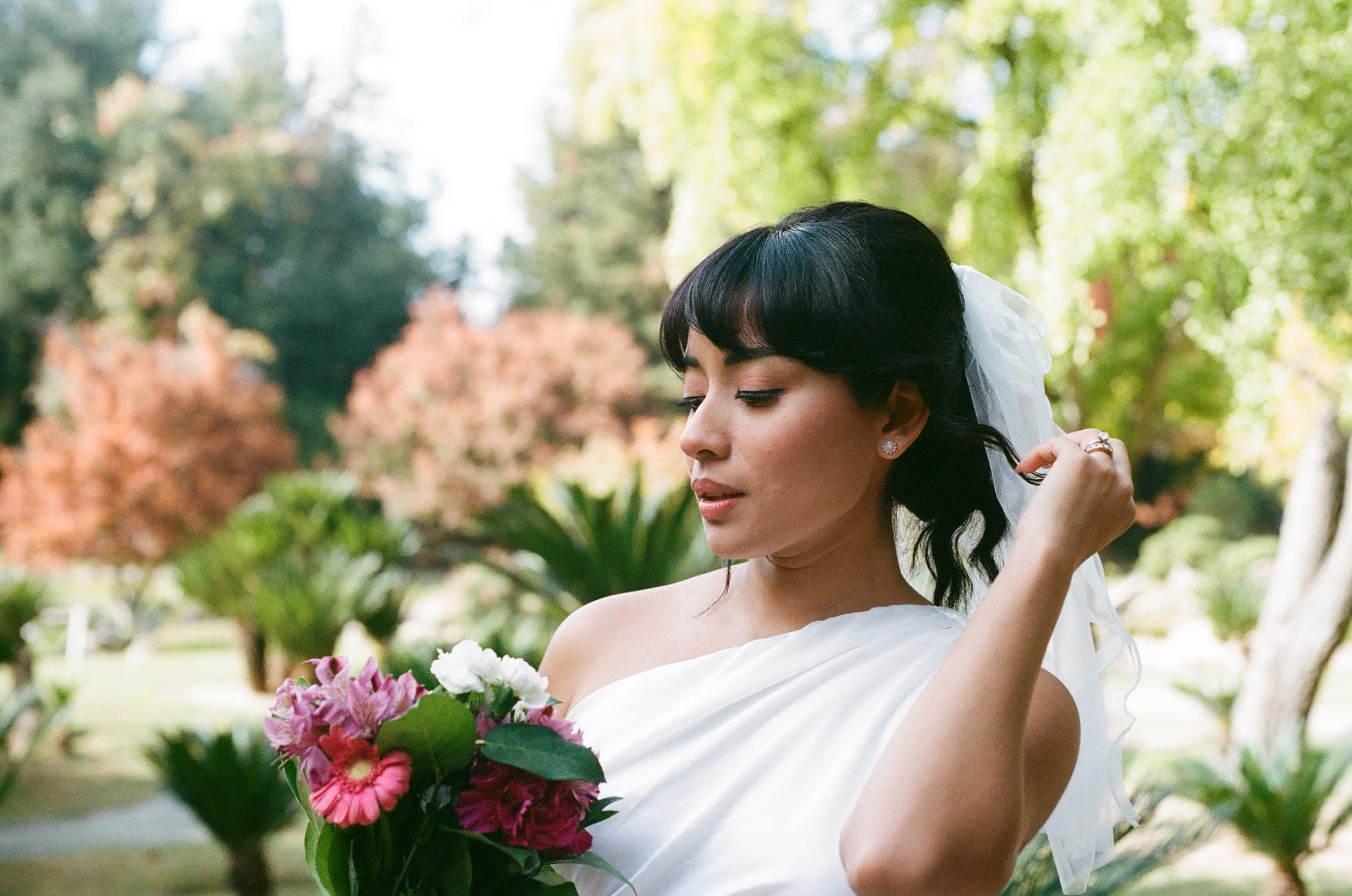 Soft 35mm film portrait of a bride with her bouquet in a sunlit garden