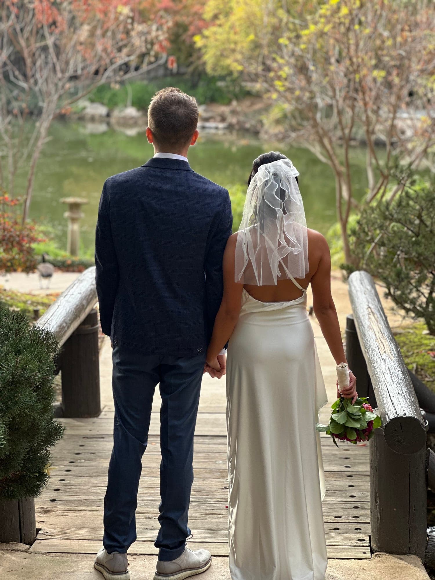 Bride and groom holding hands, looking out over the garden pond together