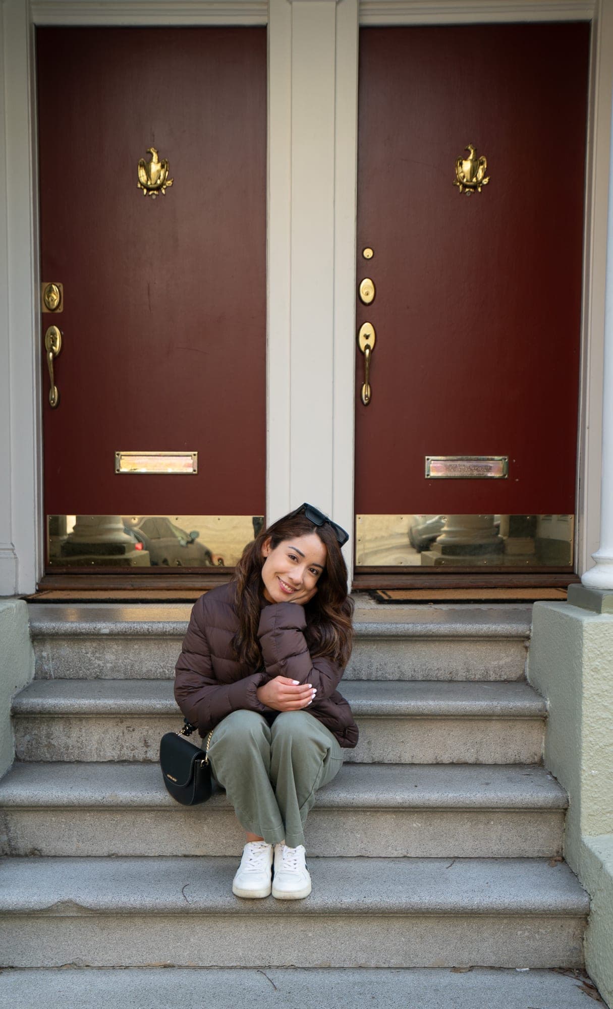 Woman seated on stone steps between two oxblood-red Victorian doors