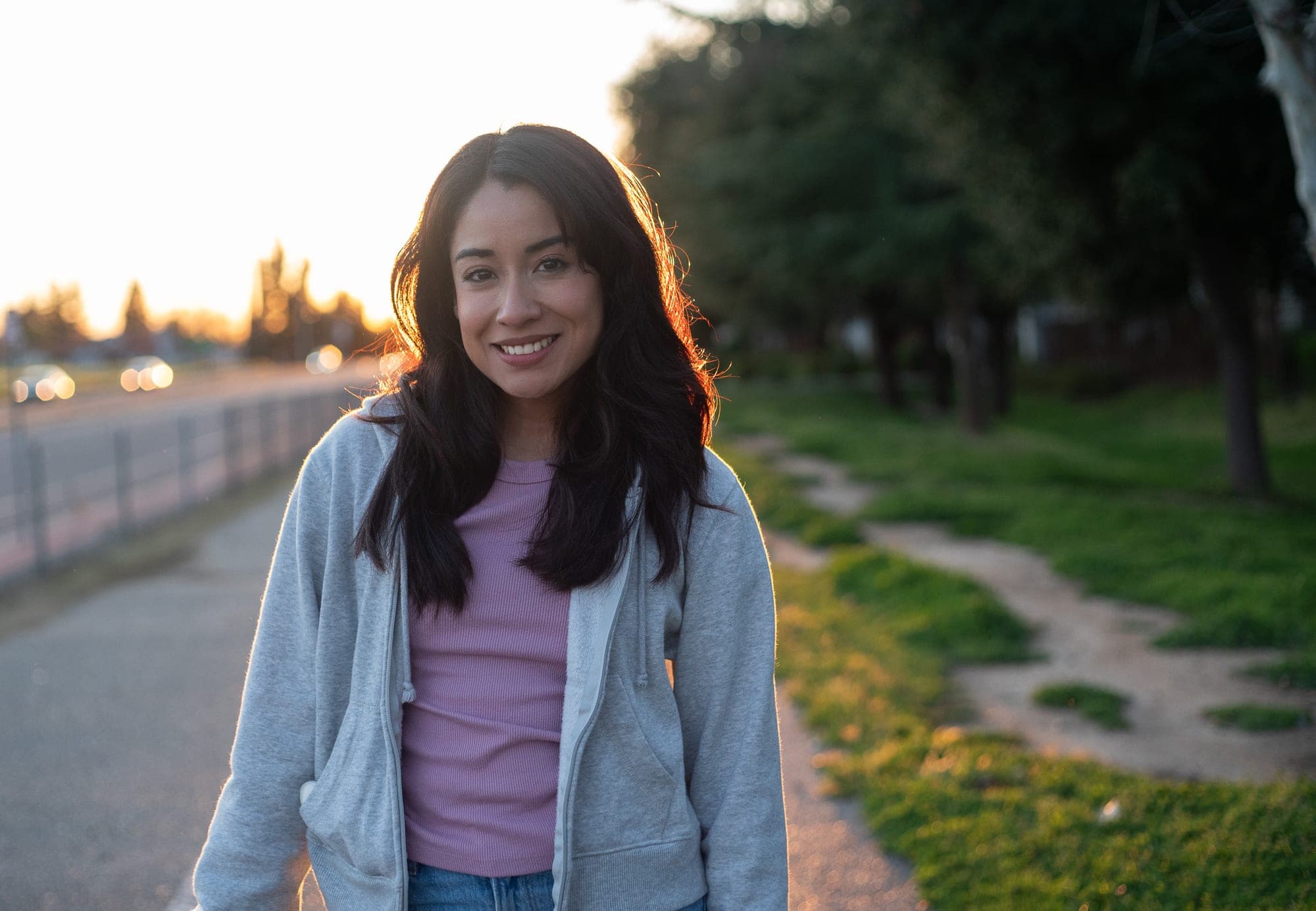 Backlit golden-hour portrait of a smiling woman on a tree-lined Fresno sidewalk