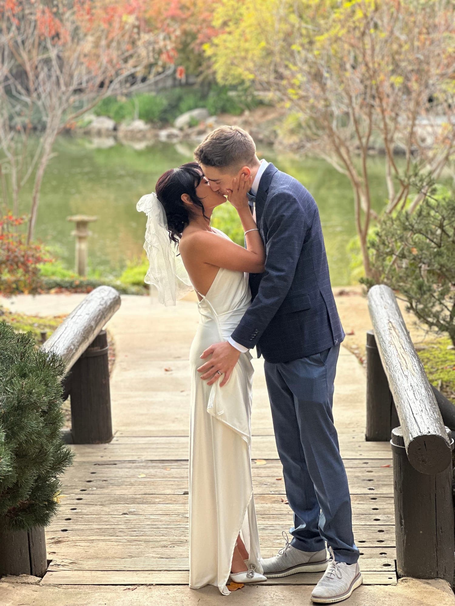 Newlyweds kissing on a garden bridge surrounded by fall color