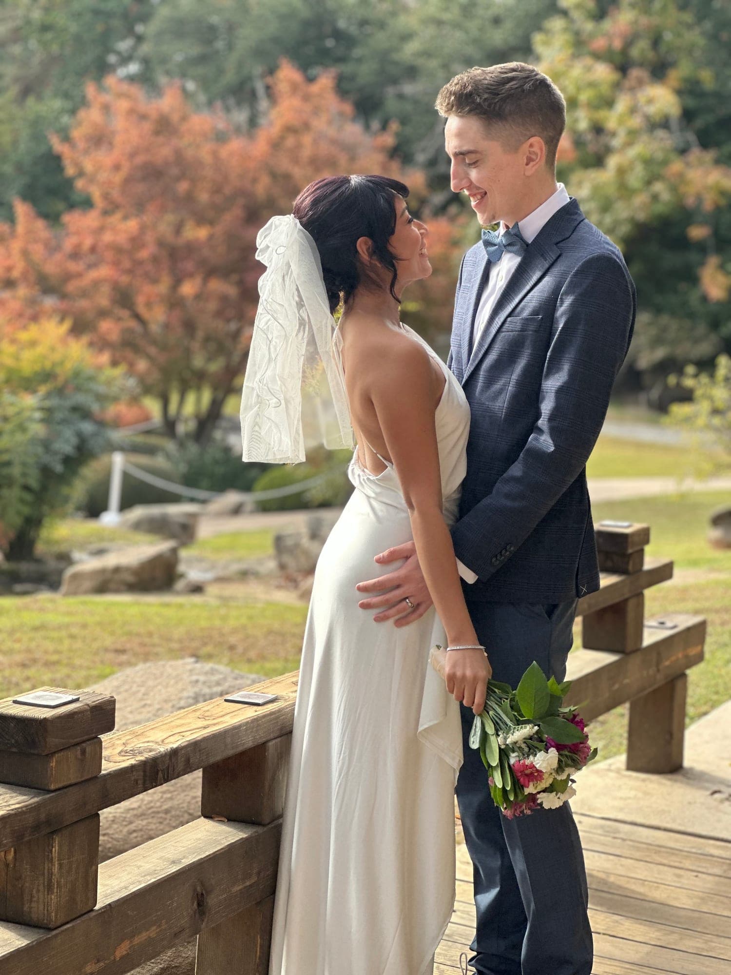 Bride and groom smiling at each other on a wooden garden bridge